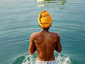 Homme de dos, torse nu avec un turban jaune sur la tête qui se baigne dans une rivière - Agrandir l'image (fenêtre modale)